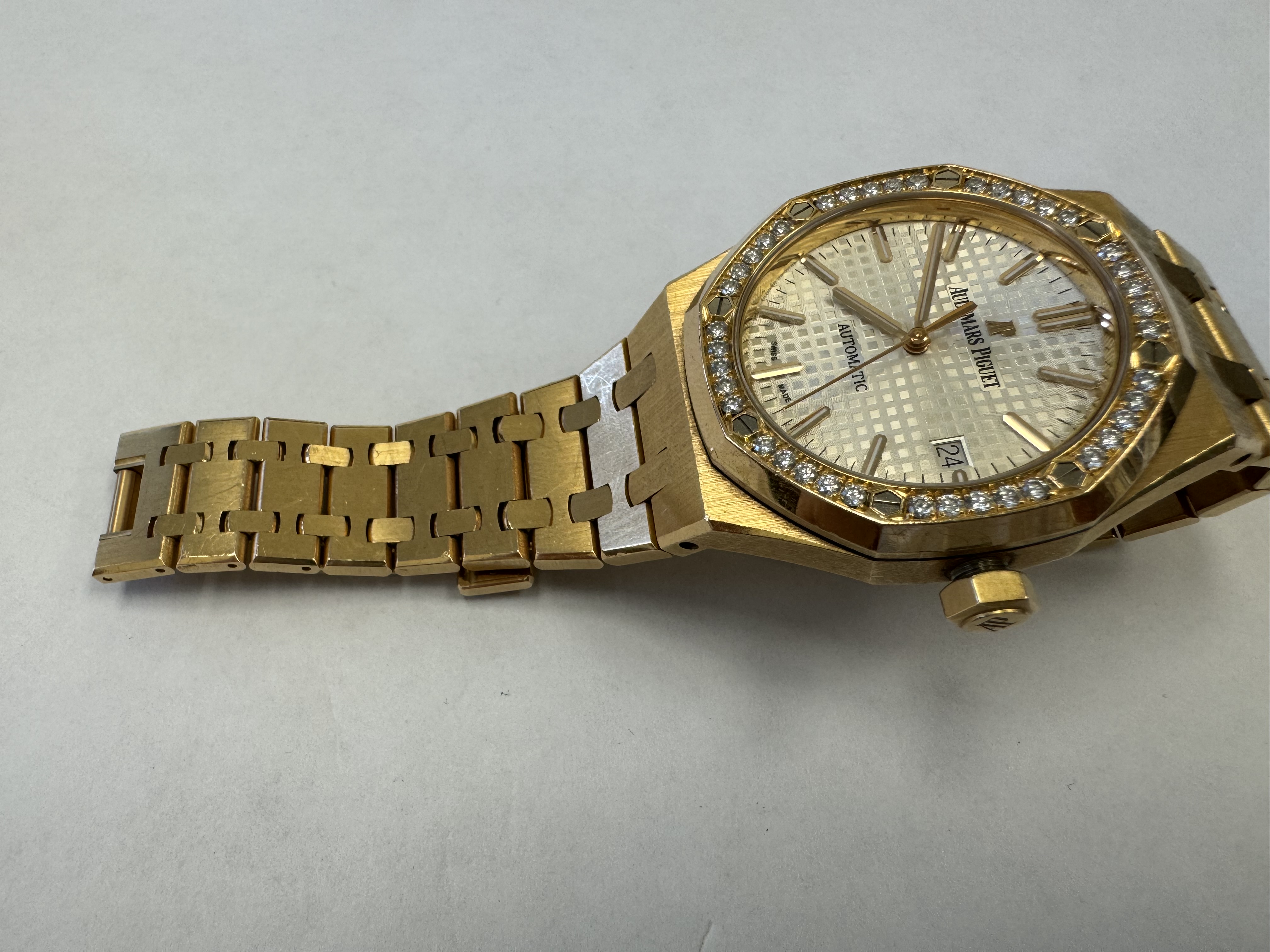Наручные часы «Audemars Piguet Royal Оаk Auto 37 Ladies ref. 15451or.zz.1256or.01»корпус ромбовидный, из металла золотистого цвета со вставкой из прозрачных камней по кругу, браслет из металла золотистого цвета с замком. На оборотной стороне штампованная надпись «ROYAL OAK», «№ 1163», «I 24742», «Au750», б/у.
