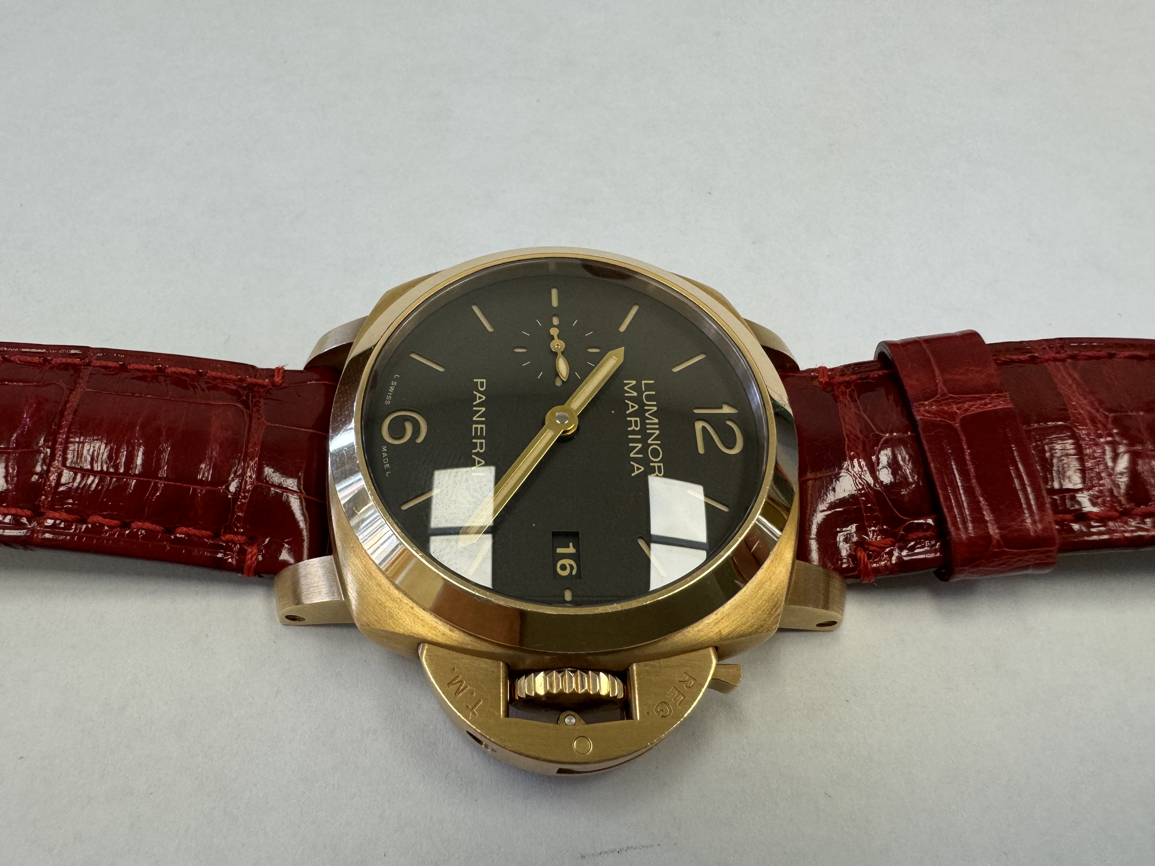 Наручные часы «Panerai Luminor Marina 1950 З Days ref. РАМ00З9З»»,корпус круглый, из металла золотистого цвета, ремешок из материала красного цвета с замком из металла золотистого цвета. На оборотной стороне штампованная надпись «OFFICINE PANERA», «0 130/500», «BB1538538», «OP 6889», «Au750», «50m», б/у