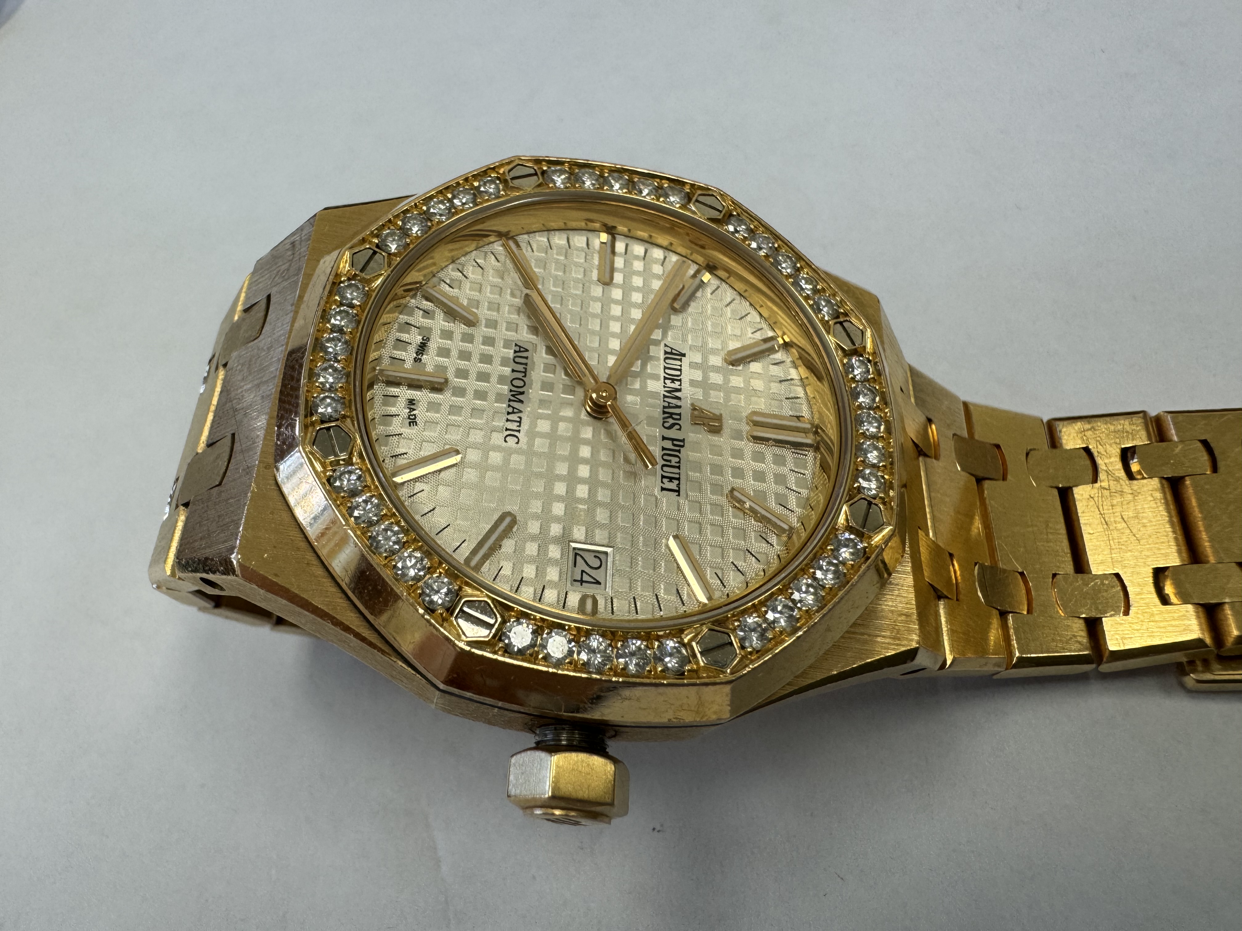 Наручные часы «Audemars Piguet Royal Оаk Auto 37 Ladies ref. 15451or.zz.1256or.01»корпус ромбовидный, из металла золотистого цвета со вставкой из прозрачных камней по кругу, браслет из металла золотистого цвета с замком. На оборотной стороне штампованная надпись «ROYAL OAK», «№ 1163», «I 24742», «Au750», б/у.