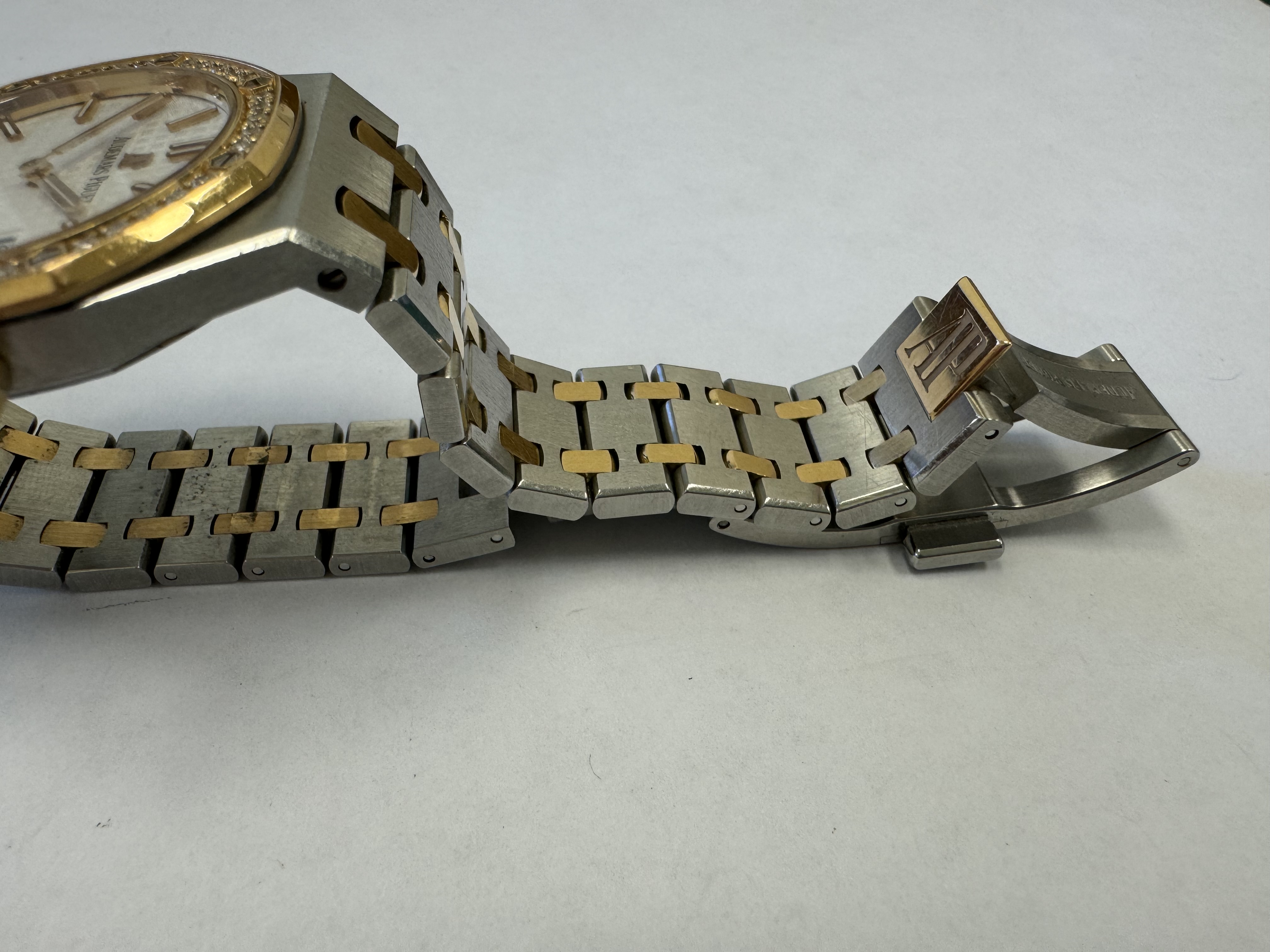 Наручные часы «Audemars Piguet Royal Оаk Quartz Ladies 67651SR.ZZ.1261SR.01», корпус ромбовидный, из металла серебристого цвета со вставкой золотистого цвета; по кругу — вставка из прозрачных камней. Браслет из металла серебристого цвета со вставками золотистого цвета с замком. На оборотной стороне штампованная надпись «ROYAL OAK», «№ 0464», «J 01230», б/у
