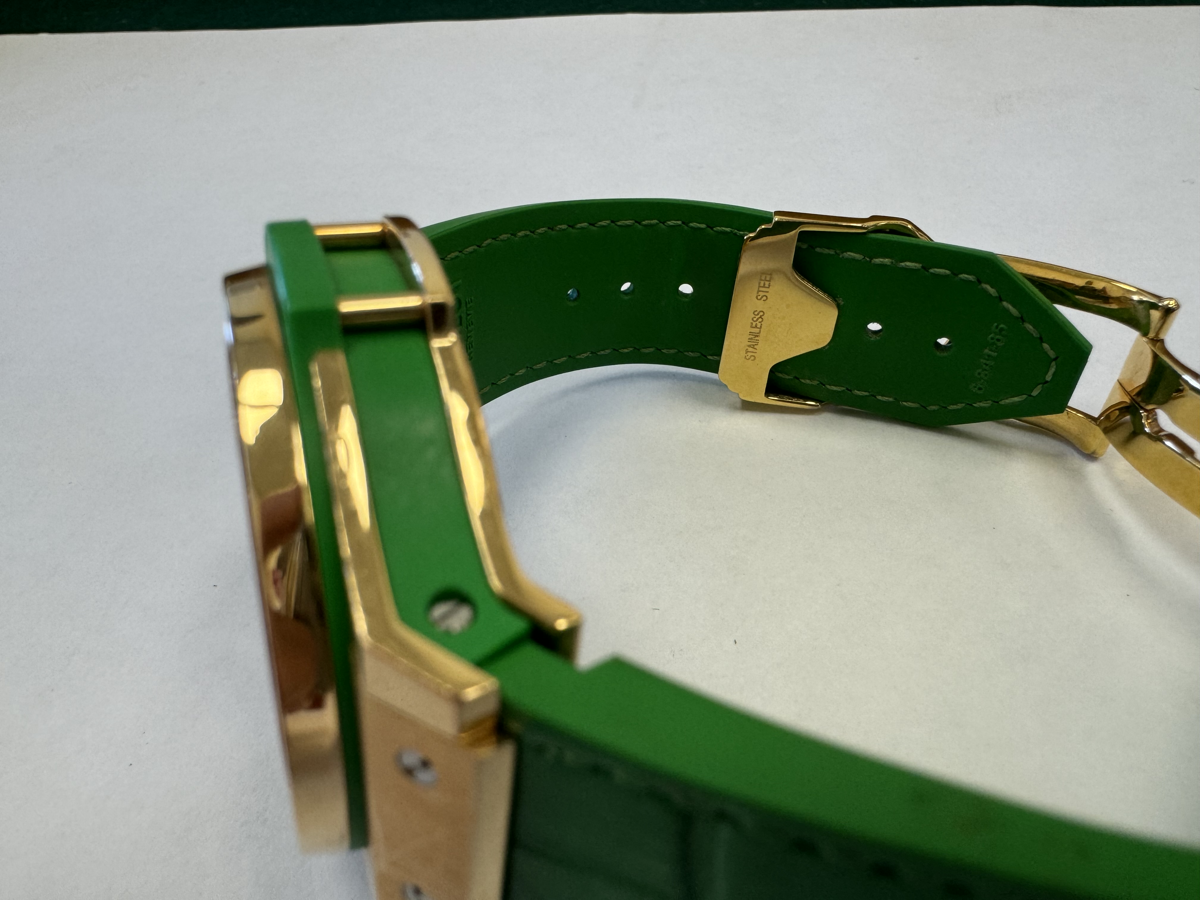 Наручные часы «Hublot Big Bang TuttiFrutti Apple ref. 341.PG.2010.LR.1922» в круглом корпусе из металла золотистого цвета с вставками зеленого цвета и камнями зеленого цвета по кругу. Часы имеют ремешок из материала зеленого цвета с замком из металла золотистого цвета. На оборотной стороне часов имеется штампованная надпись «HUBLOT», «BIG BANG», «341», «896995», «Gold 750», б/у.