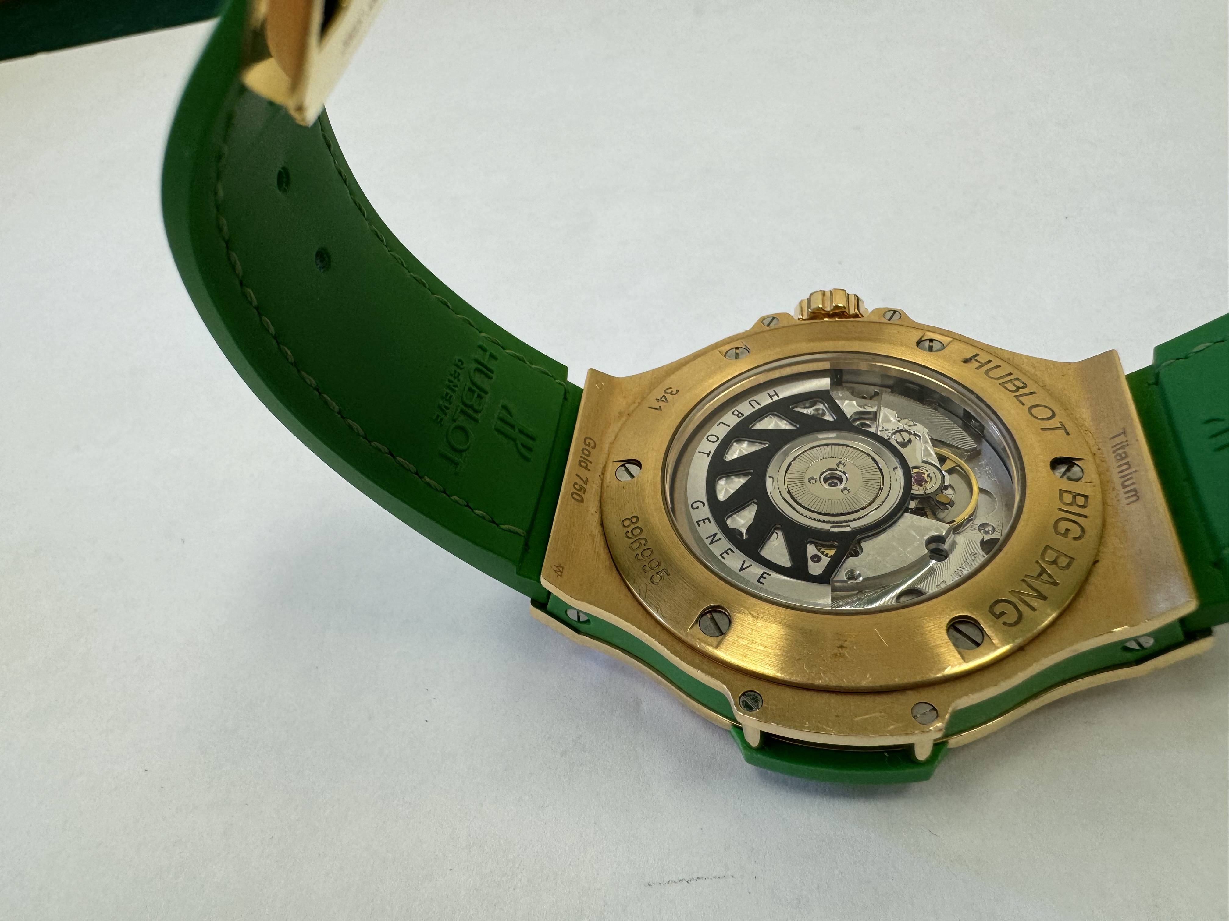 Наручные часы «Hublot Big Bang TuttiFrutti Apple ref. 341.PG.2010.LR.1922» в круглом корпусе из металла золотистого цвета с вставками зеленого цвета и камнями зеленого цвета по кругу. Часы имеют ремешок из материала зеленого цвета с замком из металла золотистого цвета. На оборотной стороне часов имеется штампованная надпись «HUBLOT», «BIG BANG», «341», «896995», «Gold 750», б/у.