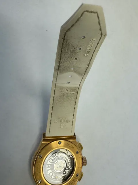Наручные часы «Hublot Classic Fusion Chronograph ref. 541.oe.2080.lr.1104»Корпус круглый из металла золотистого цвета со вставкой из прозрачных камней по кругу. Ремешок из материала белого цвета с замком из металла золотистого цвета. Маркировка на обороте: штампованная надпись «HUBLOT», «CLASSIC», "1017391", "Gold 750", б/у.
