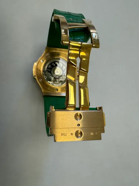Наручные часы «Hublot Big Bang TuttiFrutti Apple ref. 341.PG.2010.LR.1922» в круглом корпусе из металла золотистого цвета с вставками зеленого цвета и камнями зеленого цвета по кругу. Часы имеют ремешок из материала зеленого цвета с замком из металла золотистого цвета. На оборотной стороне часов имеется штампованная надпись «HUBLOT», «BIG BANG», «341», «896995», «Gold 750», б/у.