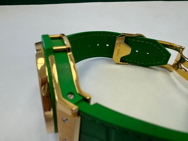 Наручные часы «Hublot Big Bang TuttiFrutti Apple ref. 341.PG.2010.LR.1922» в круглом корпусе из металла золотистого цвета с вставками зеленого цвета и камнями зеленого цвета по кругу. Часы имеют ремешок из материала зеленого цвета с замком из металла золотистого цвета. На оборотной стороне часов имеется штампованная надпись «HUBLOT», «BIG BANG», «341», «896995», «Gold 750», б/у.